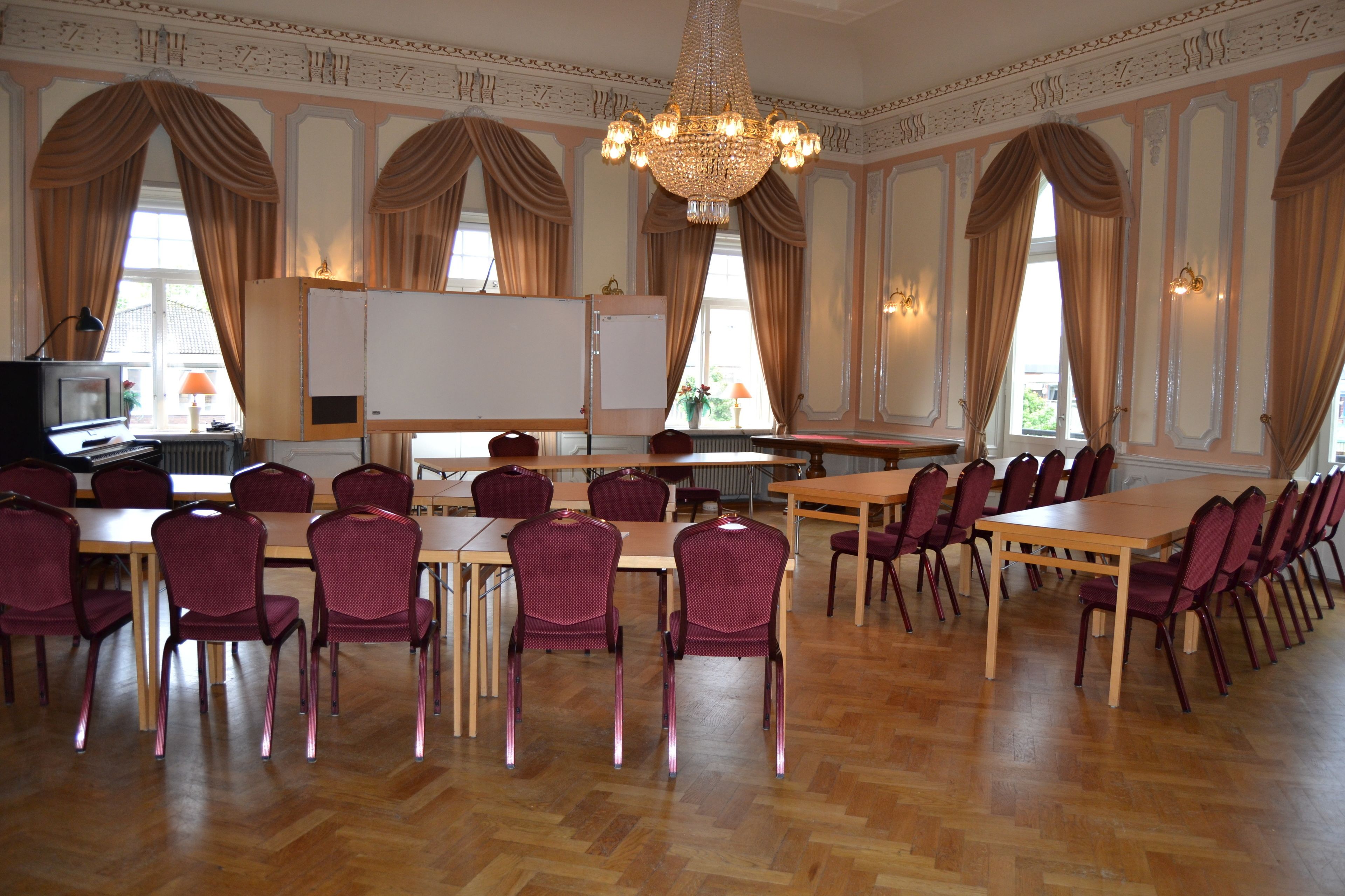 A conference room with wooden tables and chairs, a whiteboard, and a chandelier.