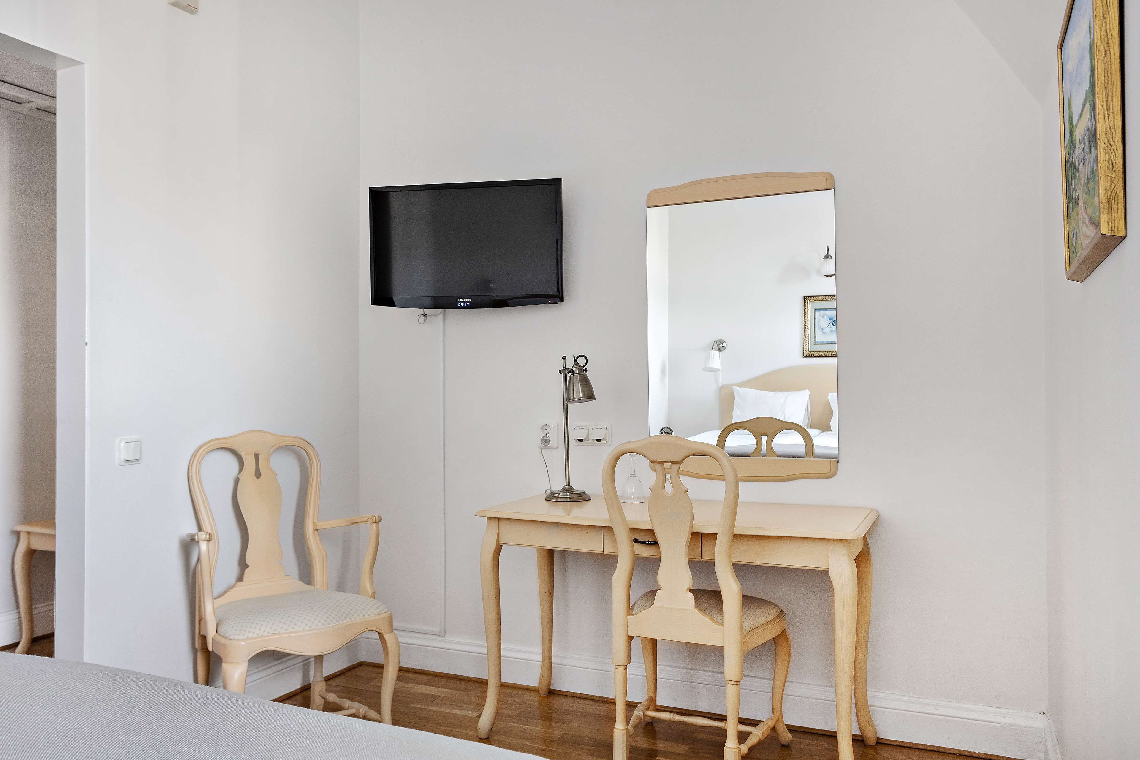 Una habitación con un escritorio de madera, dos sillas, un televisor de pantalla plana y un espejo.