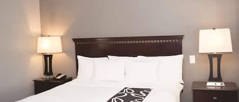 A neatly made bed with a white and black bedspread, two bedside lamps, and a dark wooden headboard.
