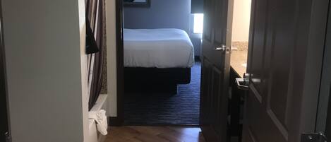 Ein Hotelzimmer mit Holzboden, einem Bett, einem Bild an der Wand und einer Tür zu einem anderen Raum.