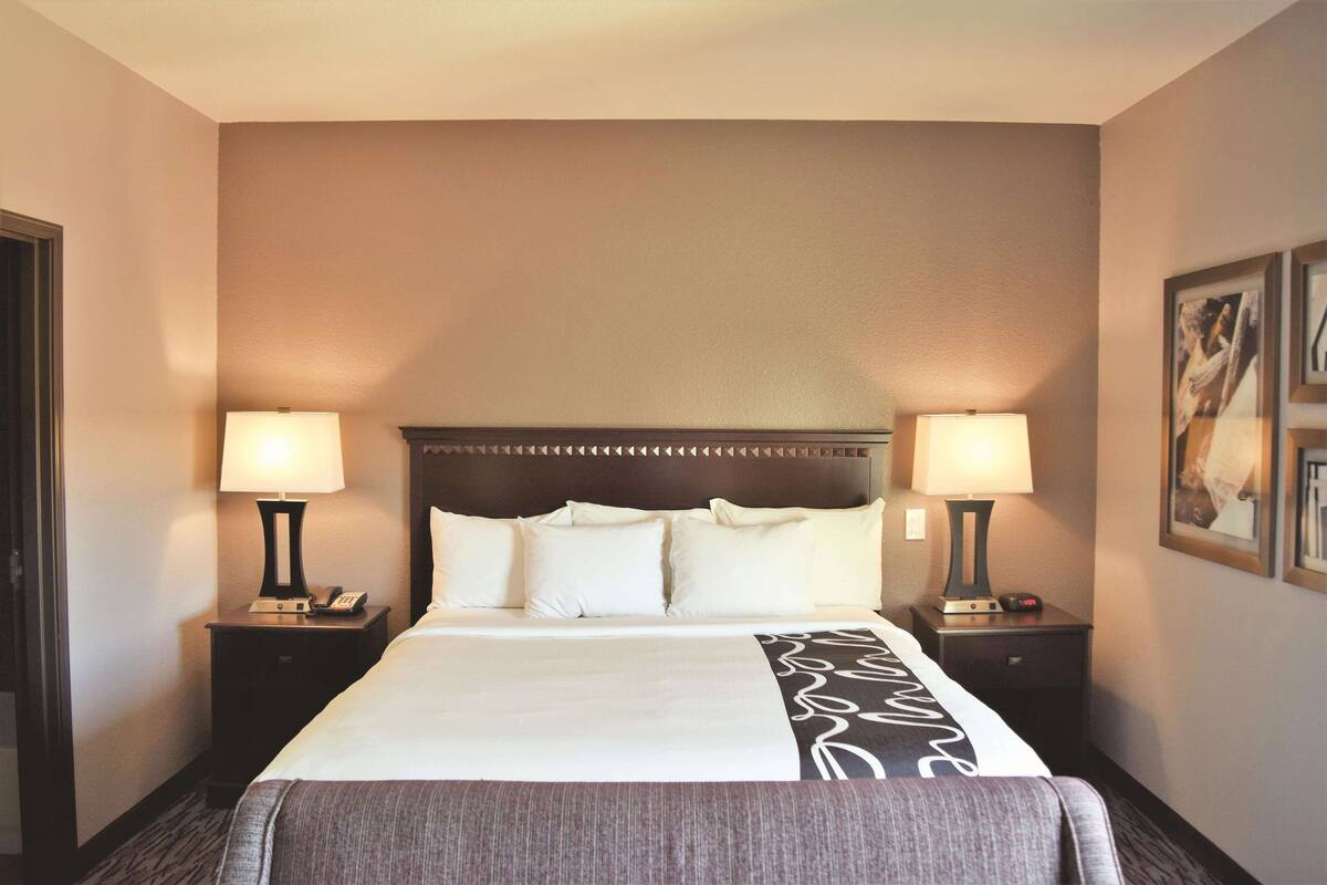 Ein Hotelzimmer mit einem großen Bett, zwei Nachttischen mit Lampen, einem hölzernen Kopfteil und gerahmten Bildern an der Wand.