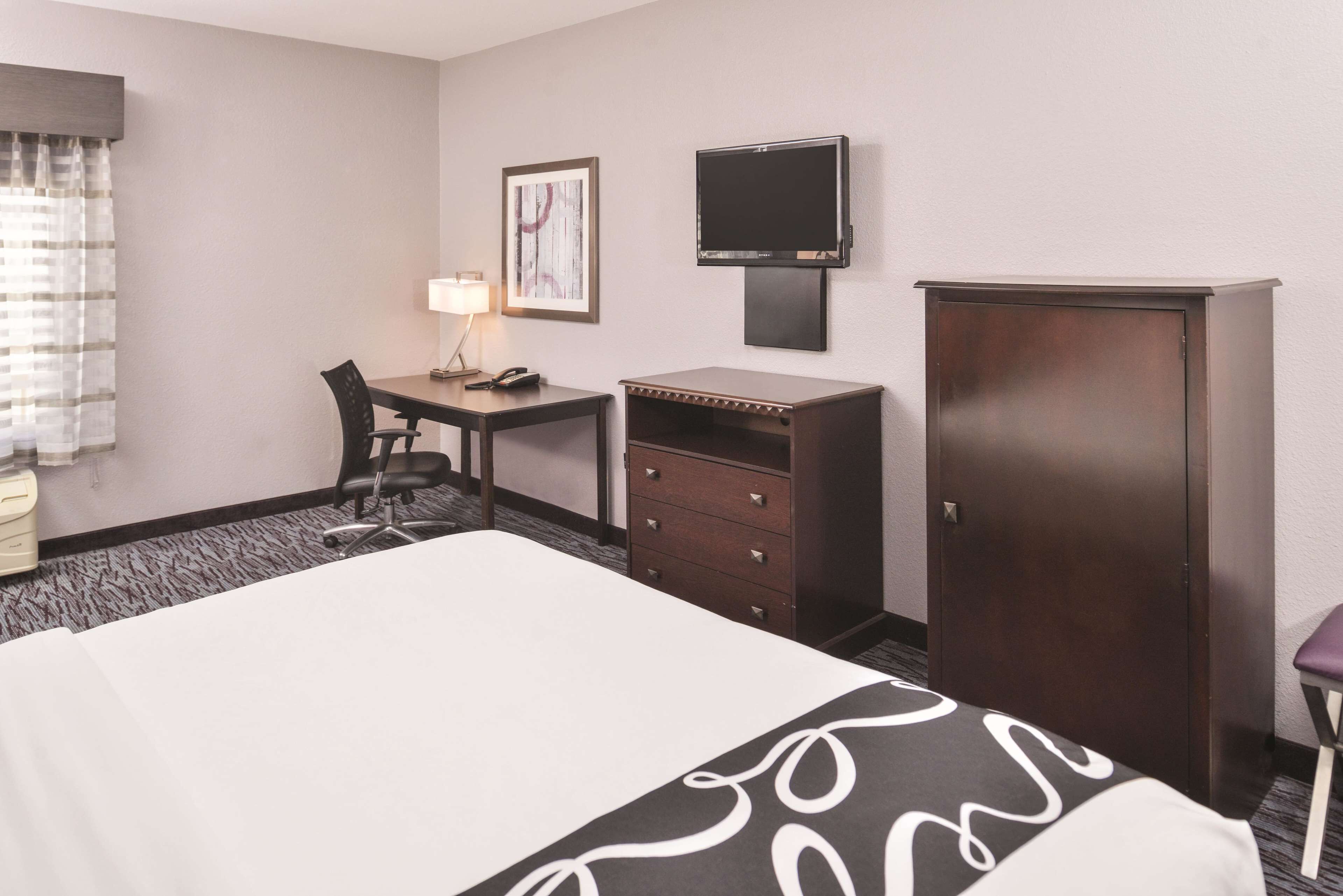 A hotel room with a bed, a desk with a chair, a TV, and a wardrobe.