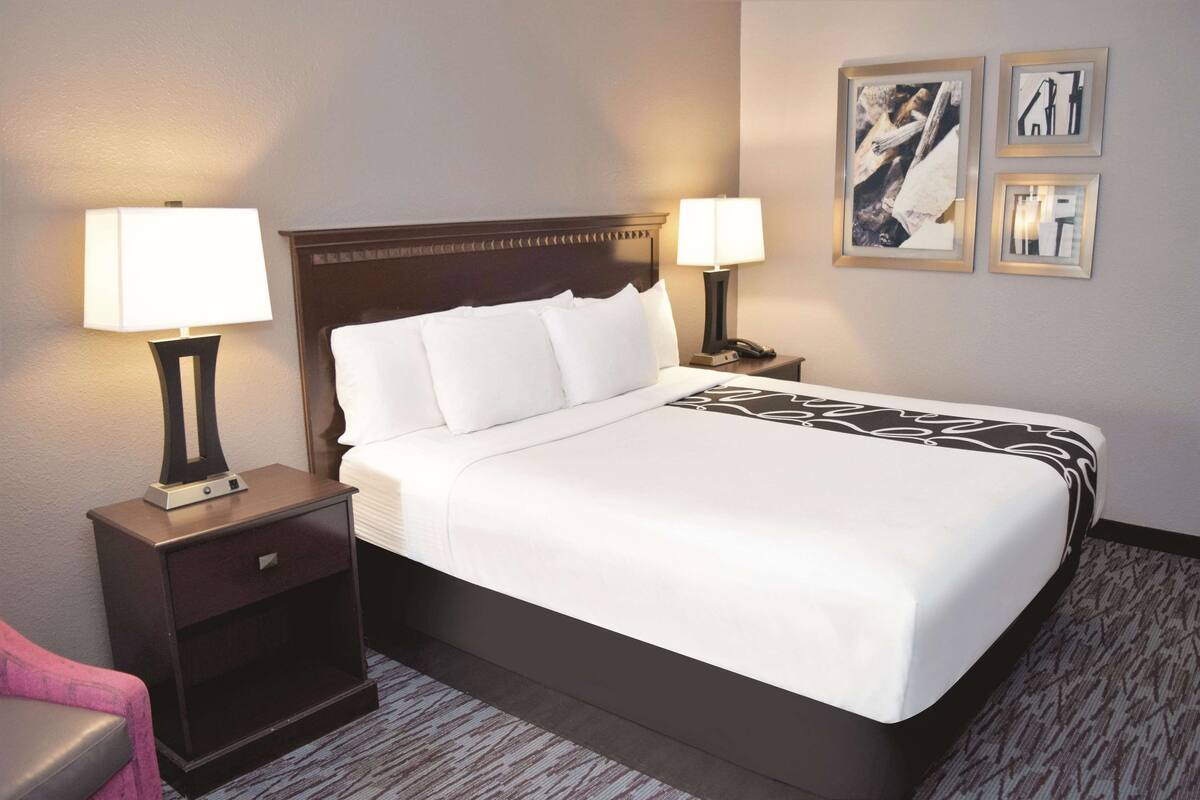 Ein Hotelzimmer mit einem großen Bett, zwei Nachttischen mit Lampen, einer kleinen Schublade und Teppichboden.
