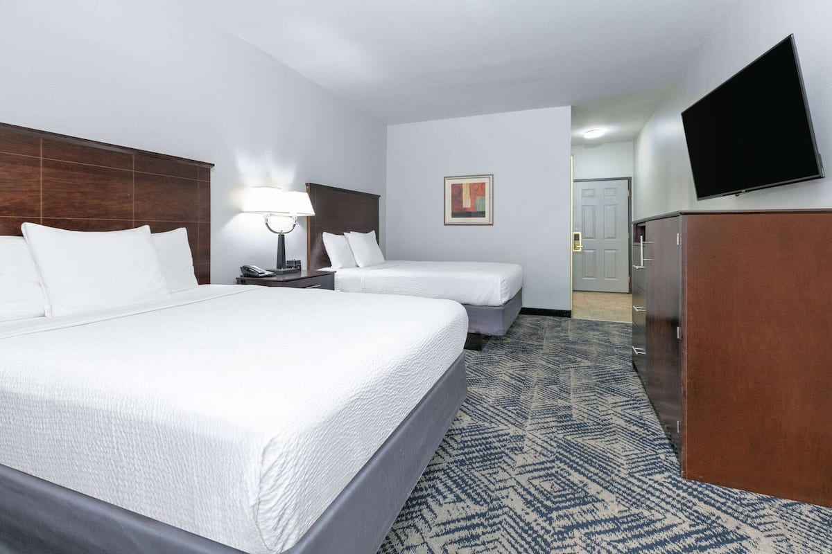 A hotel room with two beds, a desk with a lamp, a flat-screen TV, and a wardrobe.