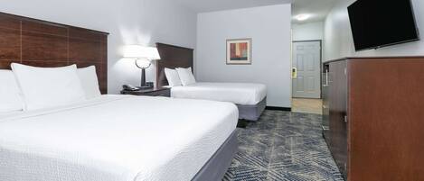A hotel room with two beds, a desk with a lamp, a flat-screen TV, and a wardrobe.