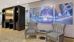 A lobby with two patterned armchairs, a reception desk, and a wall with three large cityscape paintings.