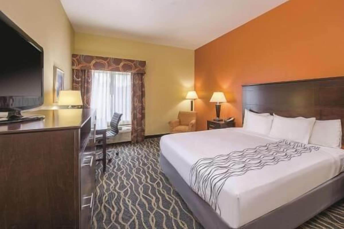 Ein Hotelzimmer mit einem Bett, einem Schreibtisch, einem Sessel, einem Fernseher und einem fenster mit Vorhängen.