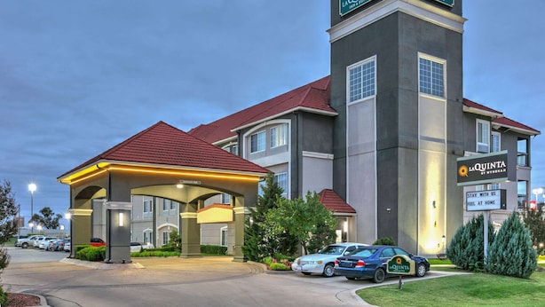 A La Quinta Inn & Suites building with a covered entrance, multiple parking spaces, and a sign indicating the name and type of the hotel.