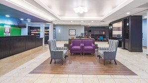 A lobby with a reception desk, two purple sofas, and patterned chairs.