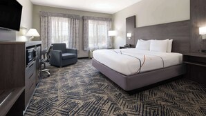 A hotel room with a large bed, a desk with a chair, a flat-screen TV, and a minibar.