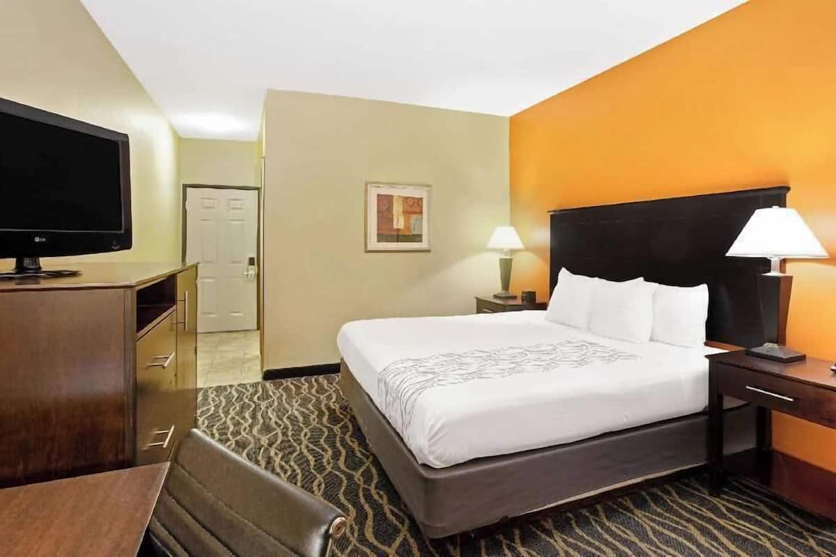 A hotel room with a bed, bedside tables, a TV, a desk, and a chair.
