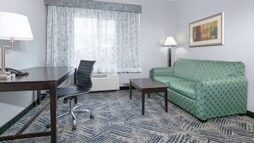 A hotel room with a desk, chair, sofa, and a patterned carpet.