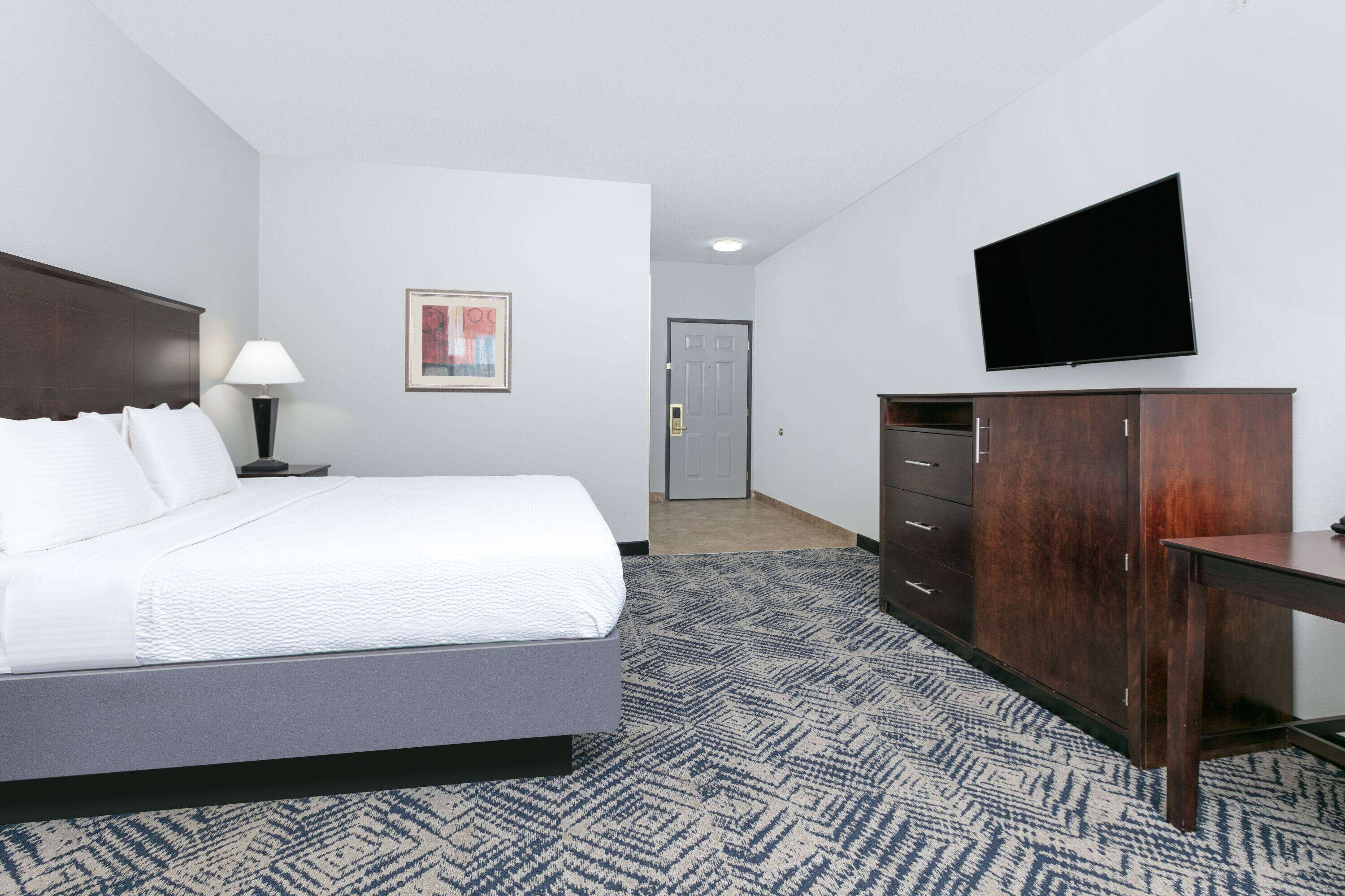 A hotel room with a bed, a desk, a television, a wardrobe, and a door.