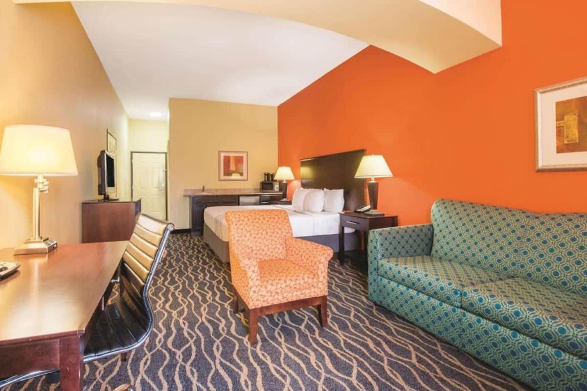 A hotel room with a bed, a desk, a chair, a sofa, and a patterned carpet.
