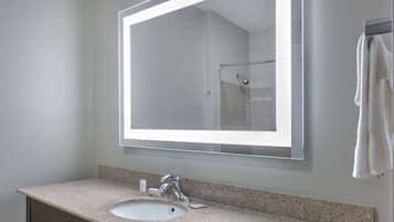 Un baño con encimera de granito, un lavamanos blanco, un espejo grande y un perchero para toallas.