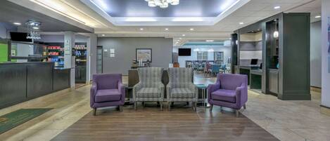 A lobby with a reception desk, purple armchairs, patterned chairs, and a dining area in the background.