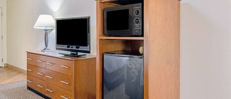 A hotel room with a wooden dresser, a television, and a refrigerator.
