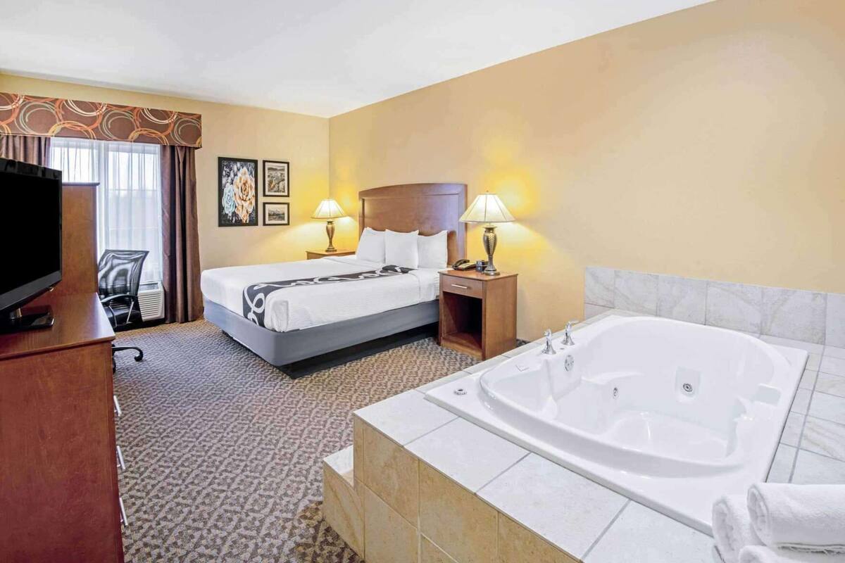 Una habitación de hotel con cama, televisión, escritorio, lámpara y bañera.