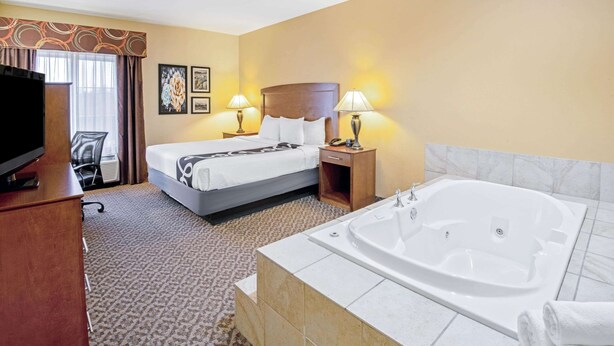 A hotel room with a large bed, a separate bathroom with a bathtub, a desk with a television, and a chair.