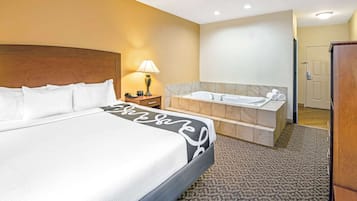 A hotel room with a large bed, a bathroom with a bathtub, and a wooden headboard.