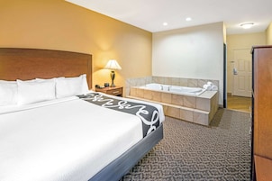 Una habitación de hotel con una cama grande, un baño con bañera y un cabecero de madera.