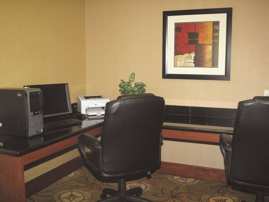 Escritório de hotel com um computador de mesa, impressora e duas cadeiras de escritório.