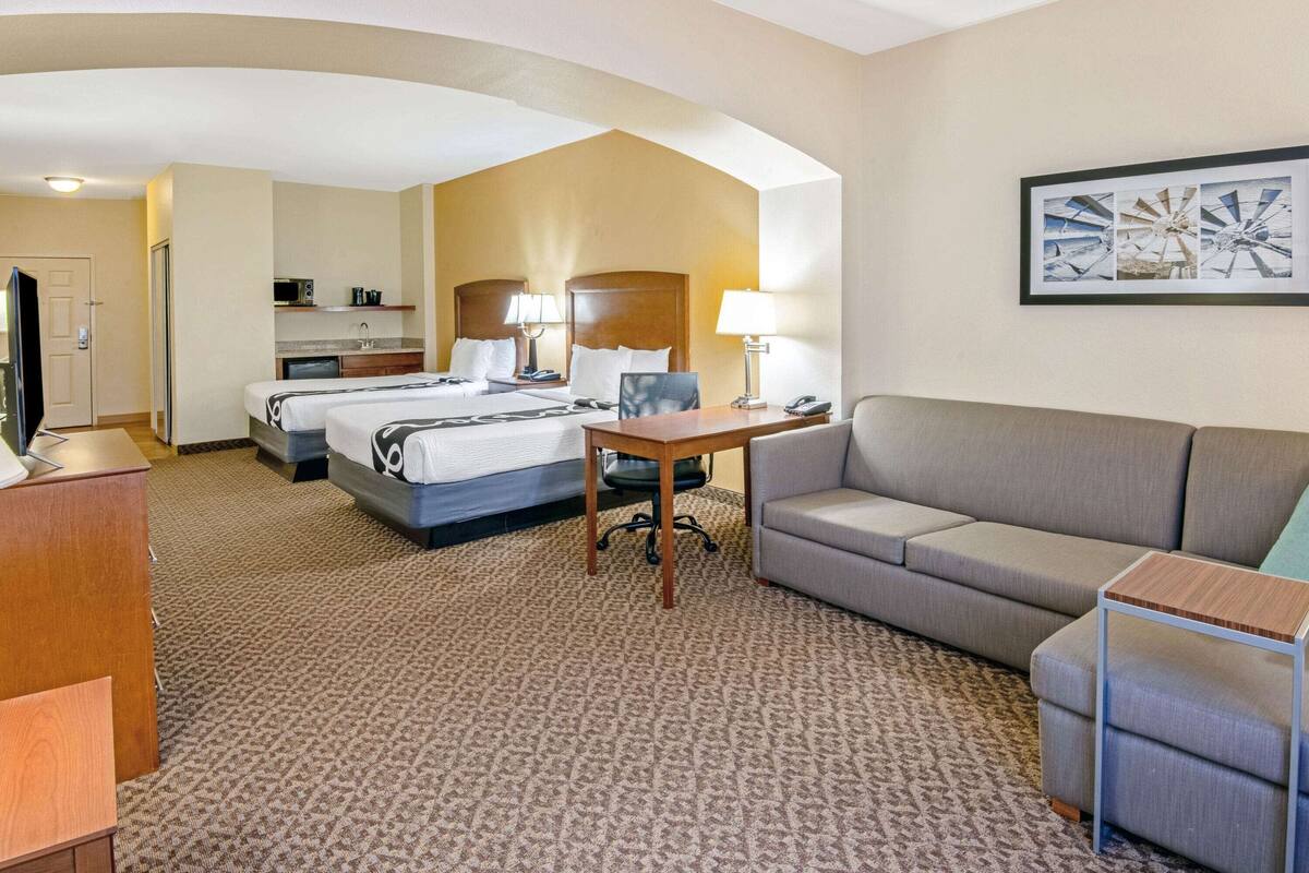 Habitación de hotel con dos camas, un sofá, un escritorio, una silla, un televisor, un microondas y un cuadro en la pared.