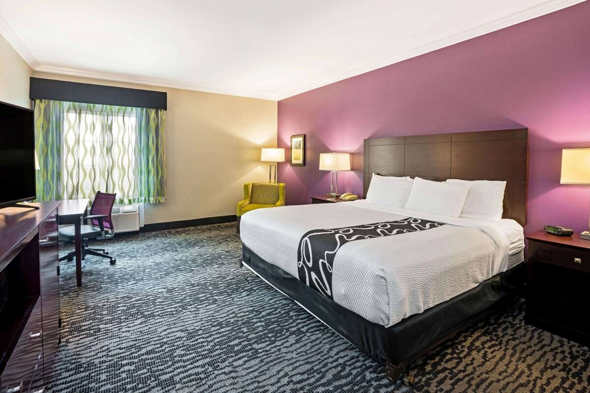 A hotel room with a bed, a desk, a chair, a TV, and two bedside lamps.