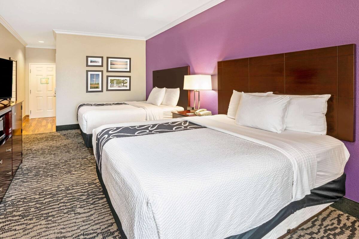 A hotel room with two beds, a television, a desk with a lamp, and framed pictures on the wall.