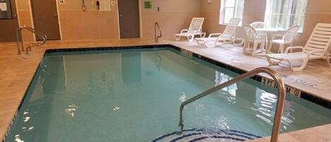 An indoor swimming pool with clear water, a diving board, and lounge chairs.