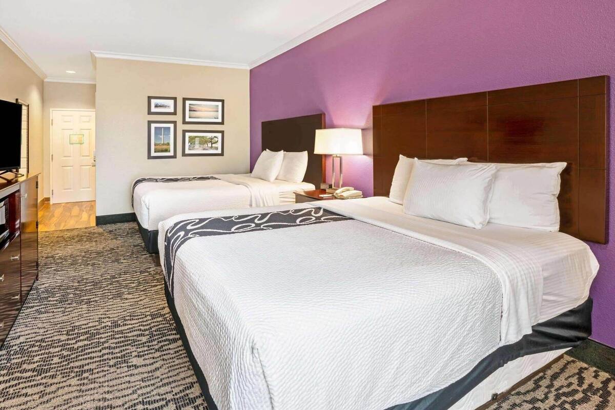 A hotel room with two beds, a TV, a desk with a lamp, and framed pictures on the wall.