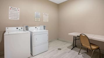 A laundry room with two white washers and dryers, a chair, and two signs on the wall.