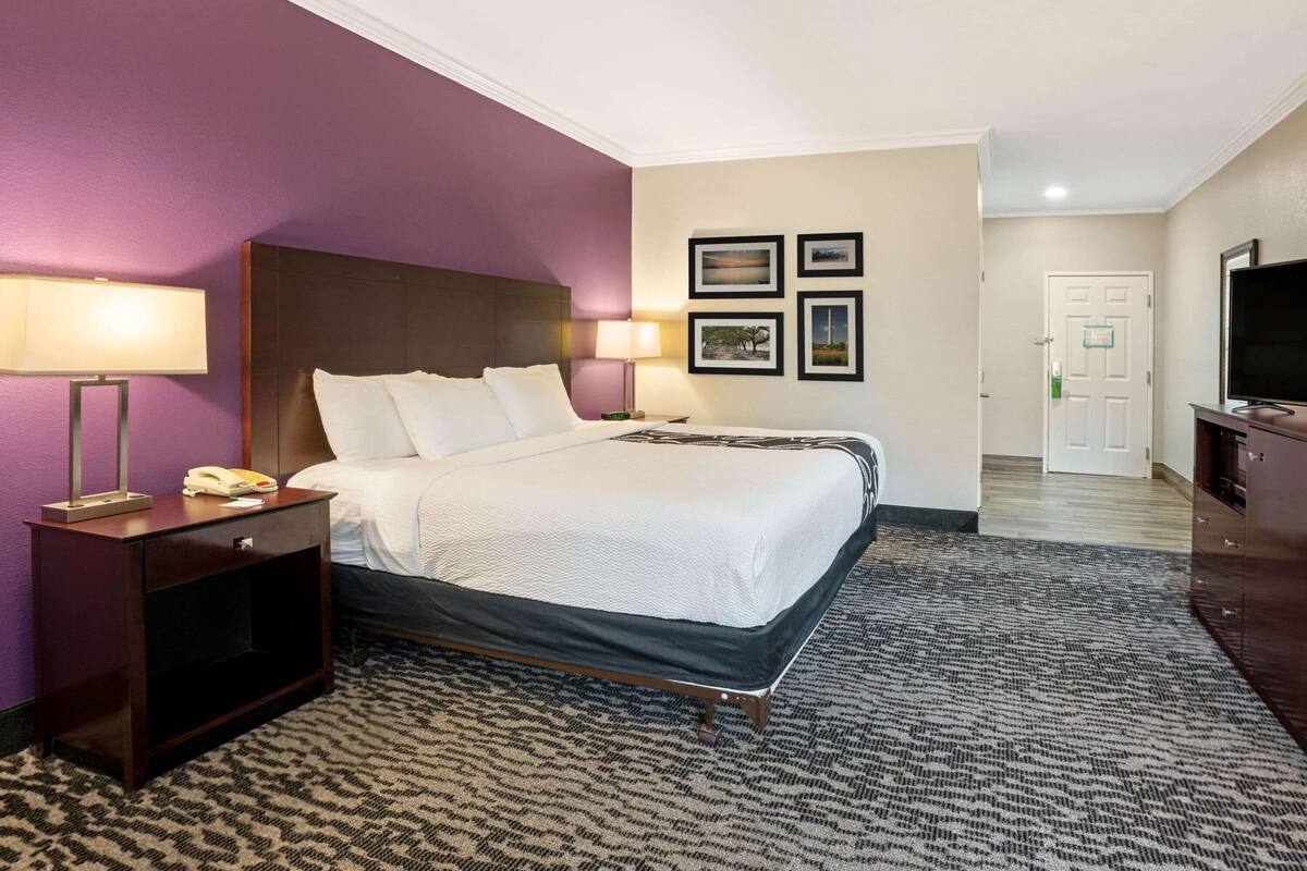 A hotel room with a bed, bedside lamps, a nightstand, a television, and framed pictures on the wall.