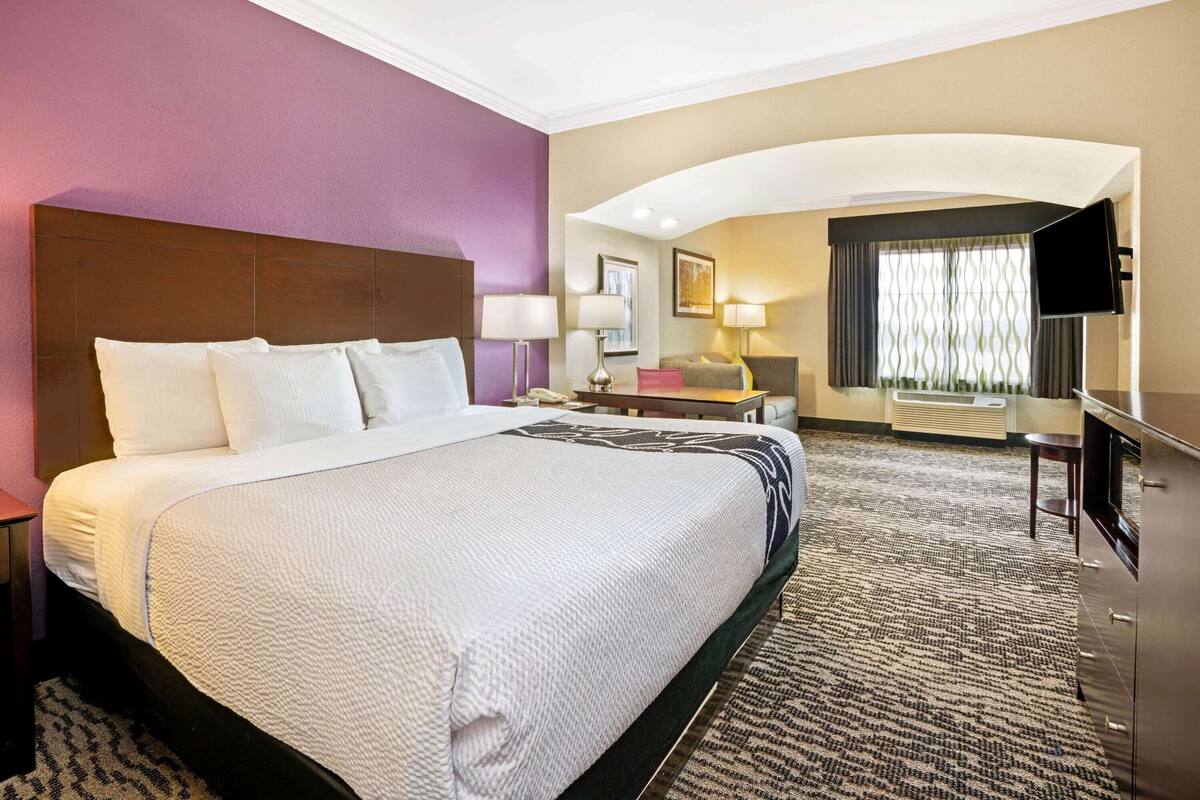 A hotel room with a large bed, a desk, a TV, and a window with curtains.