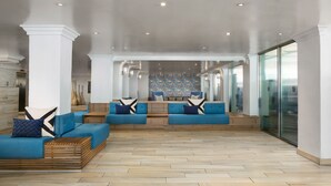 A spacious lobby with blue sofas, wooden flooring, and a view of a pool area. - Allegria Hotel (Long Beach)