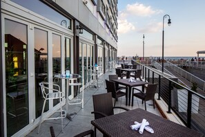 Un área de comedor al aire libre con mesas y sillas, con vista al frente marítimo.