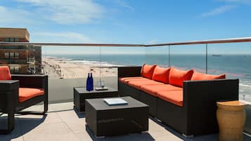 Enjoy breathtaking views of the beach and ocean from this rooftop terrace, featuring comfortable wicker furniture and a small table.