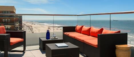 Un balcón con mobiliario de mimbre, una mesa de vidrio y vistas a la playa y al océano.