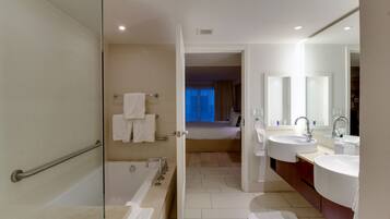 A modern hotel bathroom with a glass shower enclosure, a bathtub, two sinks, and a large mirror.