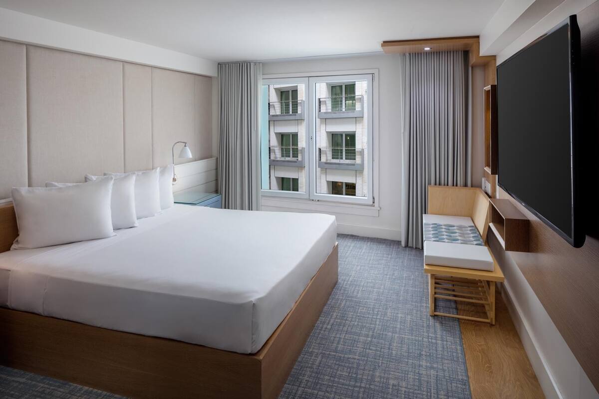 Habitación de hotel con una cama grande, televisión, una zona de estar pequeña y ventana con cortinas.