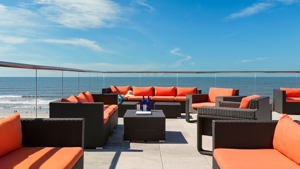 A beachside lounge with wicker furniture and orange cushions, overlooking the sea. - Allegria Hotel (Long Beach)