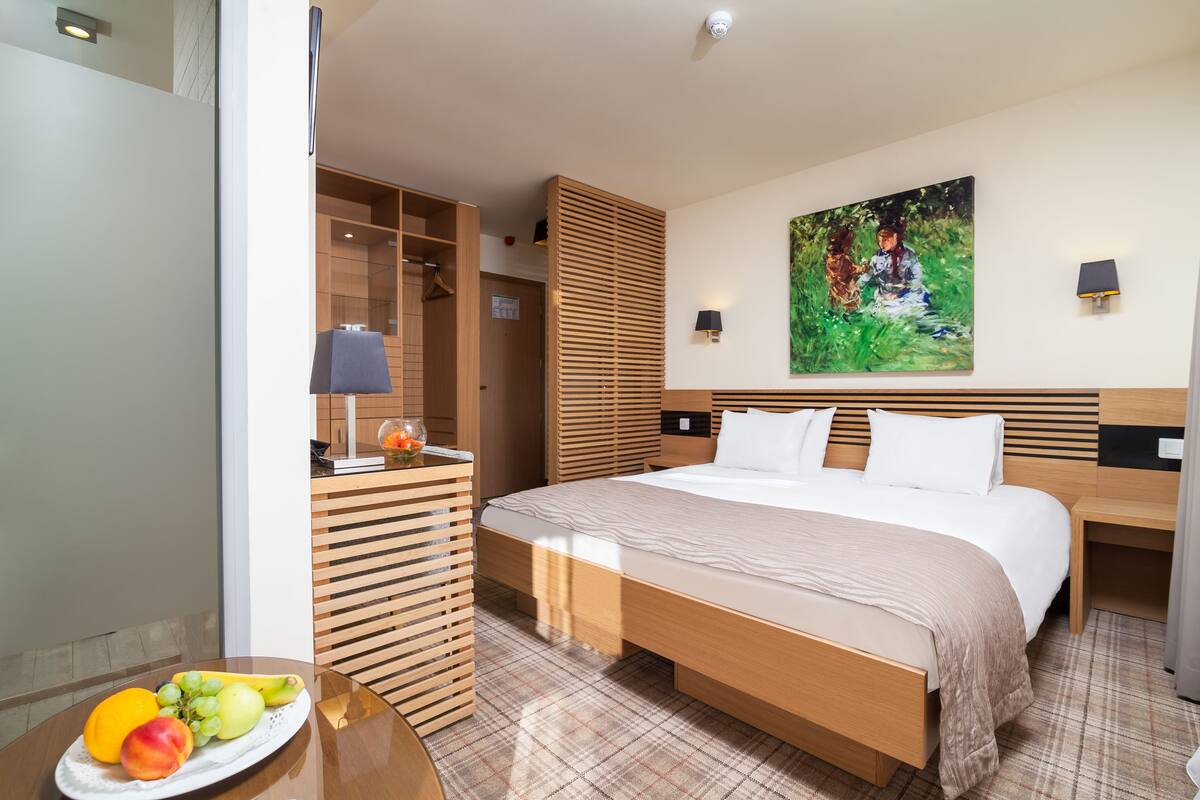 Una habitación de hotel con una cama grande, un armario de madera, un cuadro en la pared y una bandeja de frutas sobre la mesa.