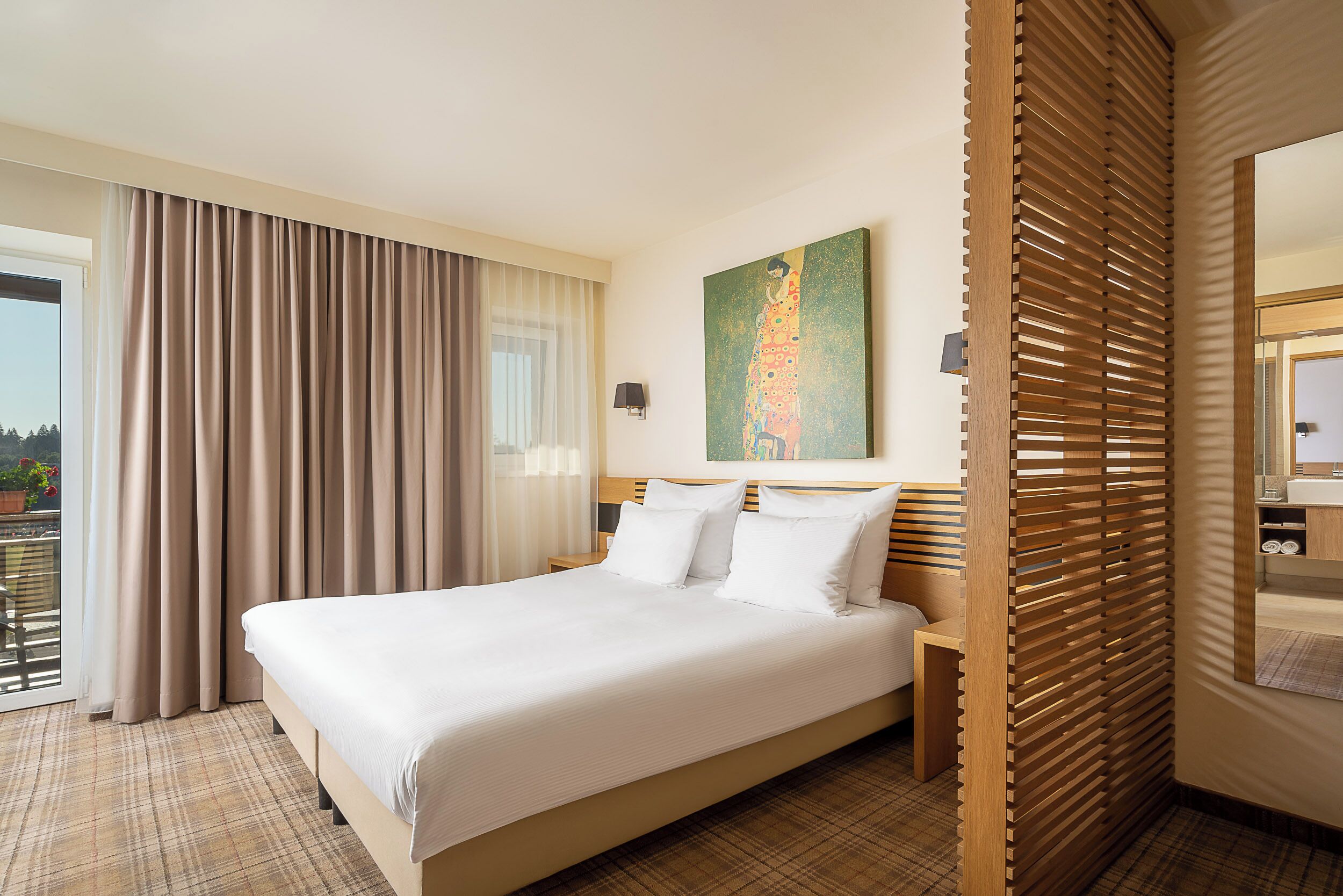 Habitación de hotel con una cama grande, un cuadro en la pared y vistas al exterior por la ventana.