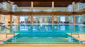 A large indoor swimming pool with clear glass sides, multiple levels with seating areas, and large windows allowing natural light. - Ana Hotels Sport Poiana Brasov (Brasov)