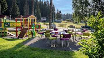 Relax and socialize in our outdoor space, featuring a playground for kids and seating areas for adults, surrounded by a scenic forest view.