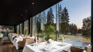 A restaurant with tables set for dining, large windows offering a view of trees and a road. - Ana Hotels Sport Poiana Brasov (Brasov)
