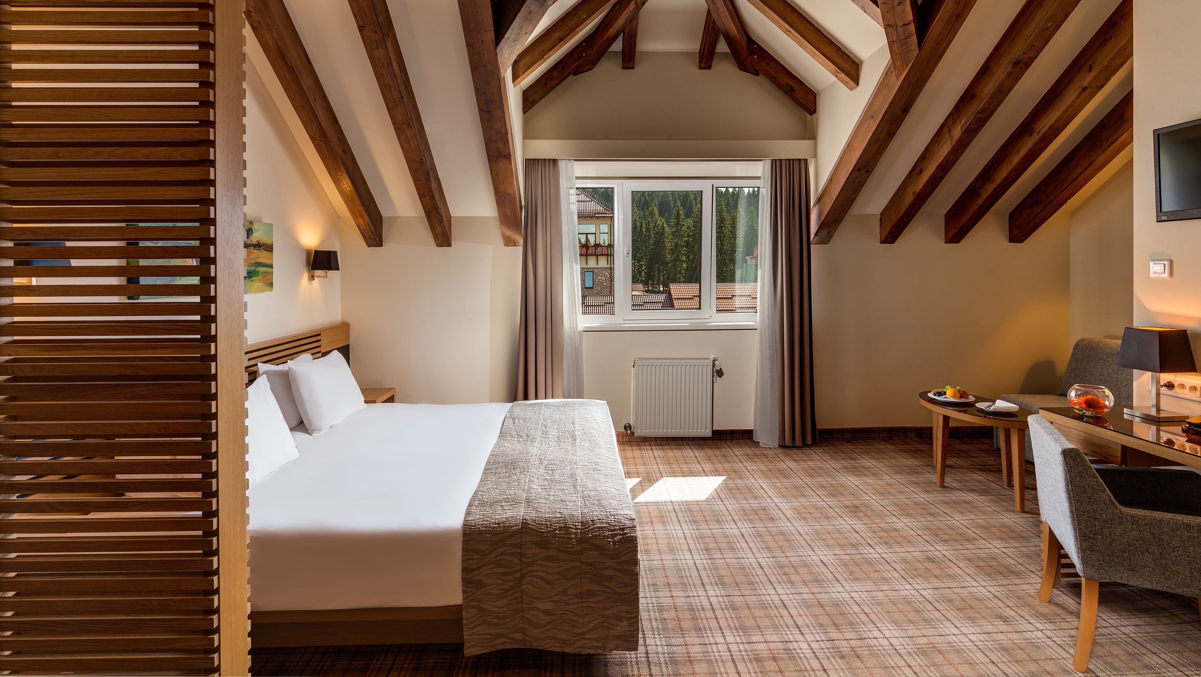 Ein Schlafzimmer mit Bett, Schreibtisch, Stuhl, Fenster und Holzbalken an der Decke.