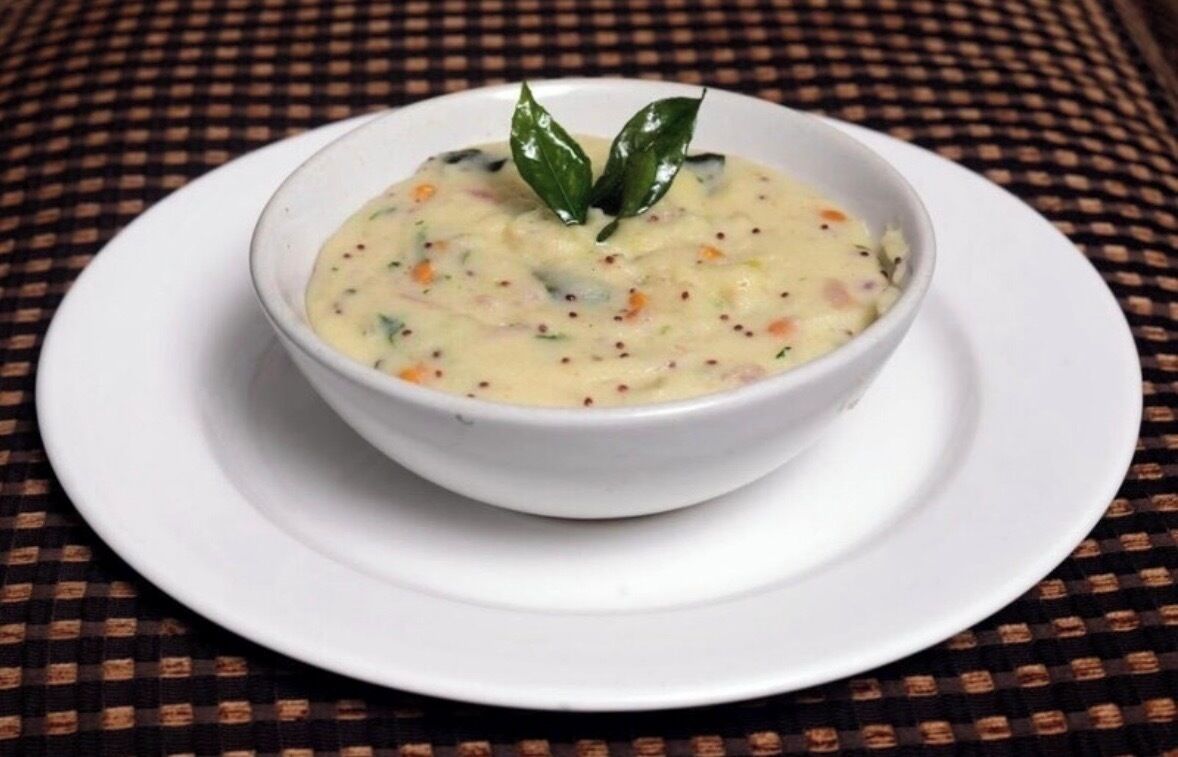 A bowl of soup on a white plate with a checkered tablecloth underneath.