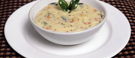 A bowl of soup on a white plate with a checkered tablecloth underneath.
