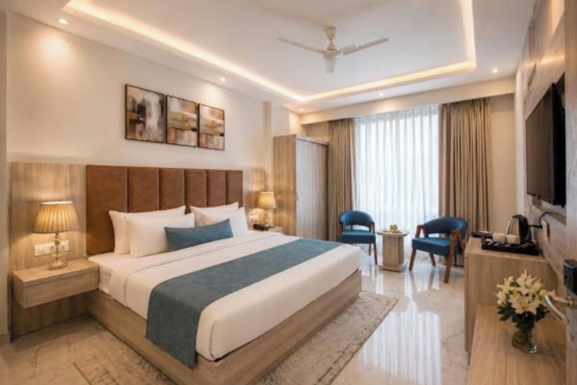 A modern hotel room with a large bed, bedside lamps, a flat-screen TV, a ceiling fan, and a view of the outdoors through the window.